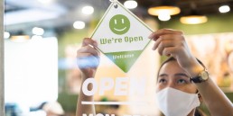 Business owner Asian woman wear protective face mask ppe hanging open sign at her restaurant / café, open again after lock down due to outbreak of coronavirus covid-19